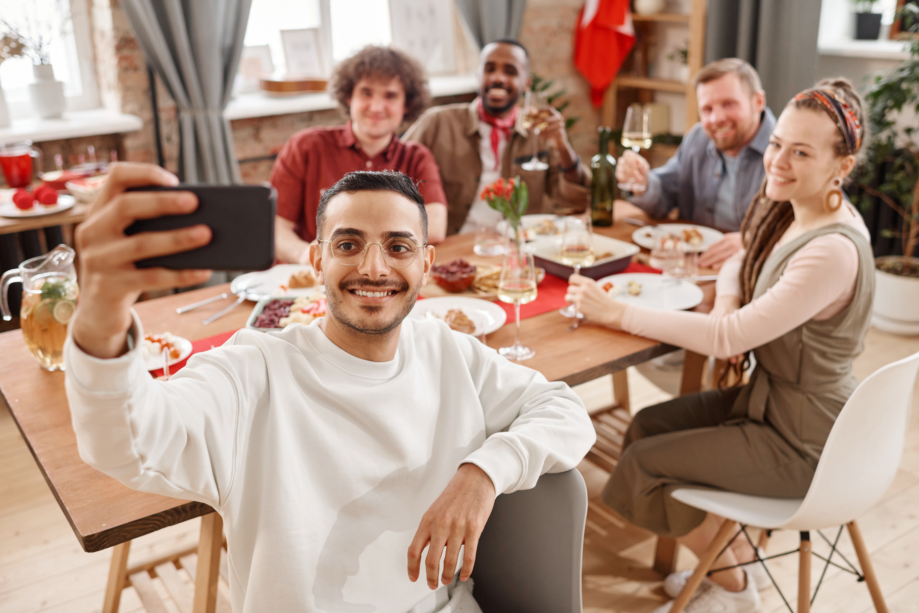 Man in White Sweater Taking a Group Picture Using Smartphone